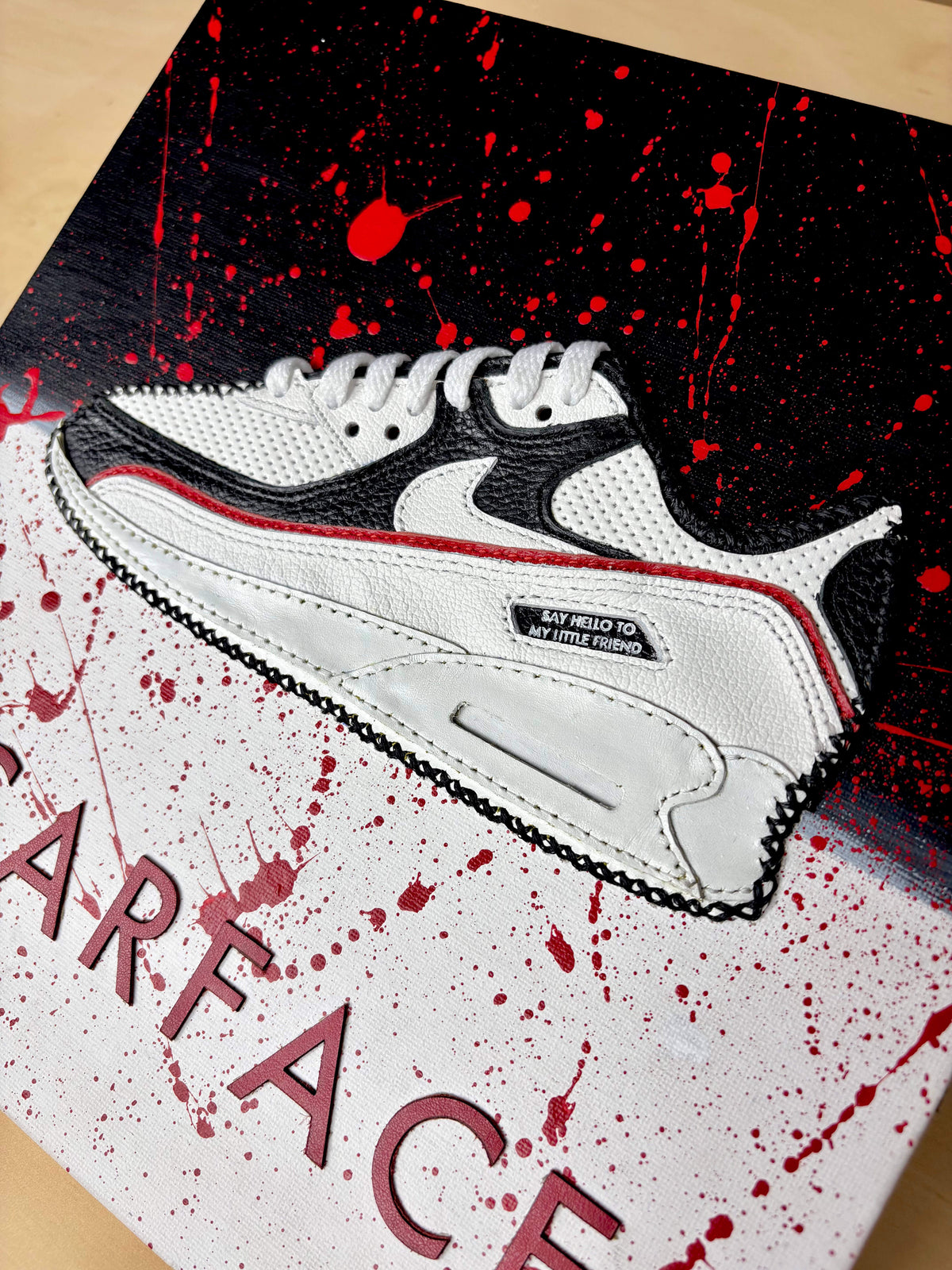 A white leather piece of sneaker artwork with black overlays and red accents, shown on a stylised black-and-white box with red paint splatter and the wording 'SCARFACE' visible.