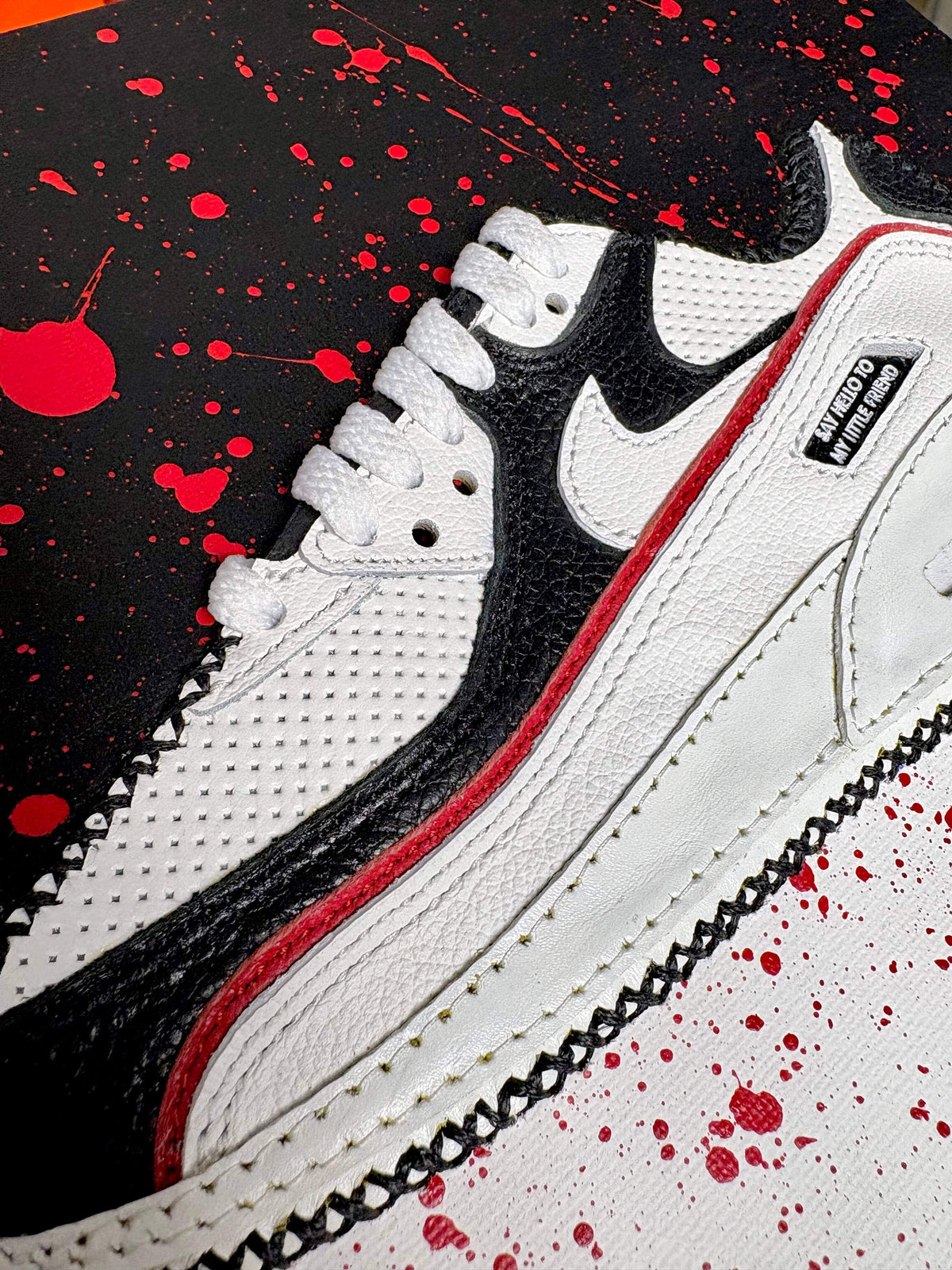 A close-up of Scarface sneaker artwork with black overlays and red accents, resting on a black background with red paint splatters.