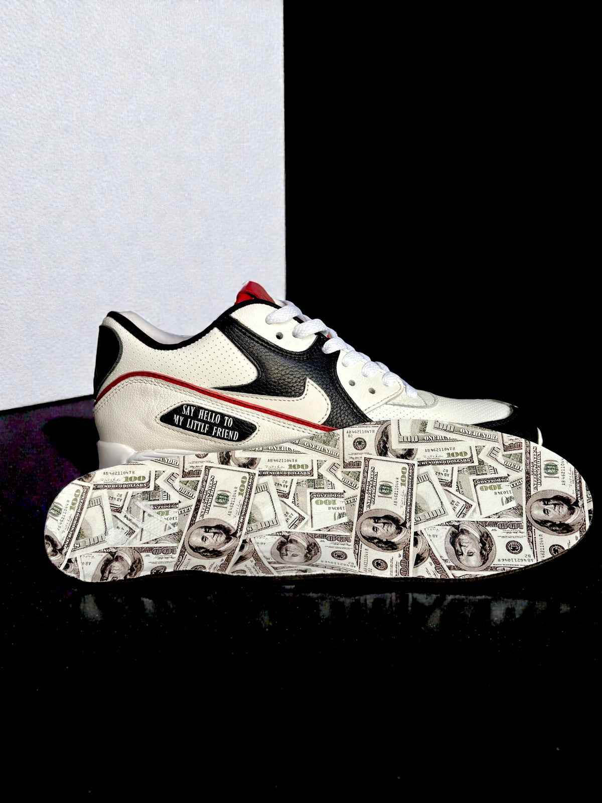 A custom Nike Air Max 90 from the side and sole. The upper is primarily white with black overlays, a red trim, custom vinyl insoles with $100 bills
